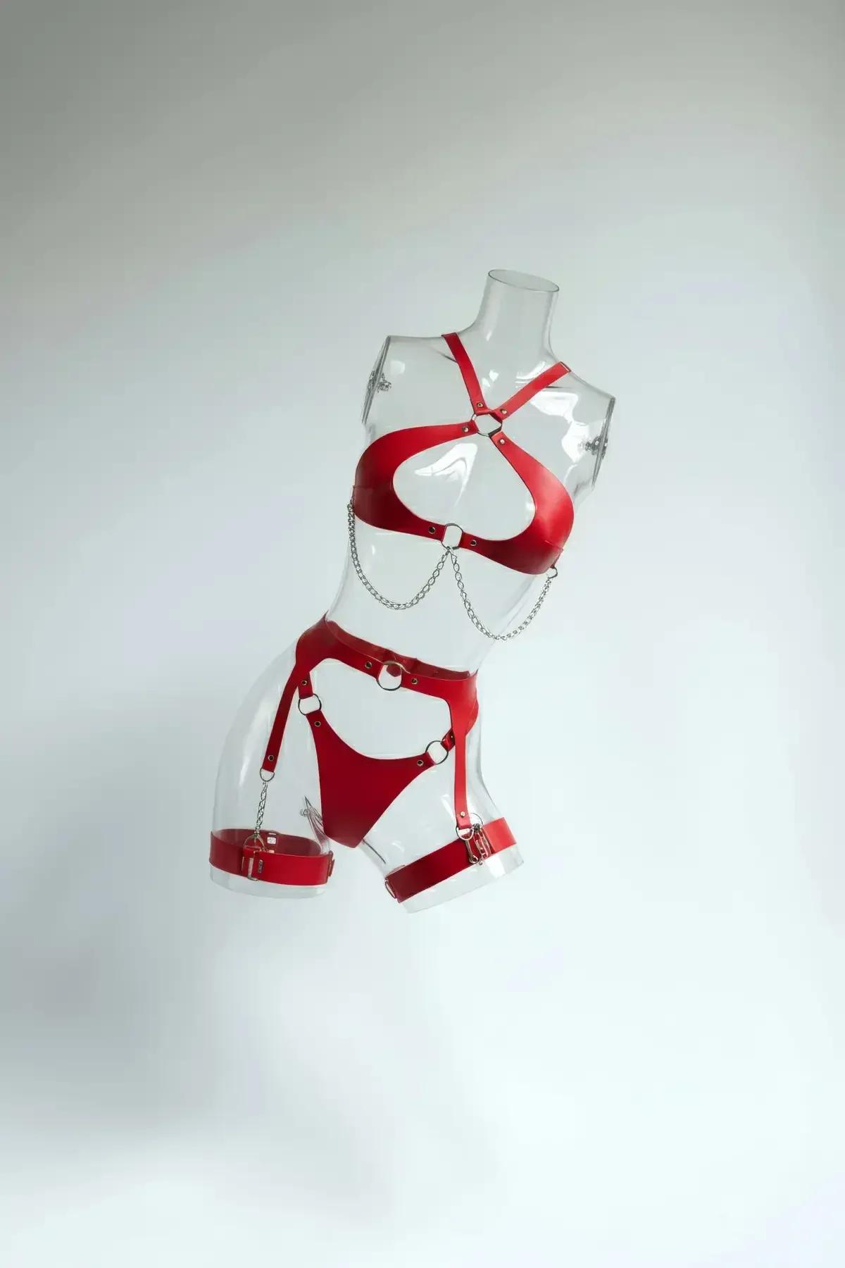 Red faux leather 3-piece harness set with silver O-rings and draped chains on clear mannequin, chest harness waist band and t