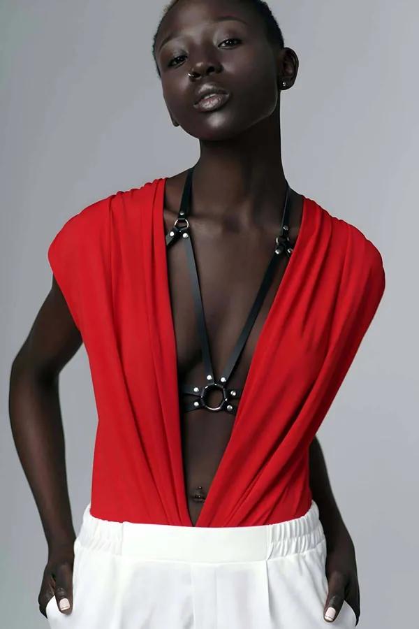 Black faux leather chest harness with silver O-ring and stud rivets worn over a red draped top