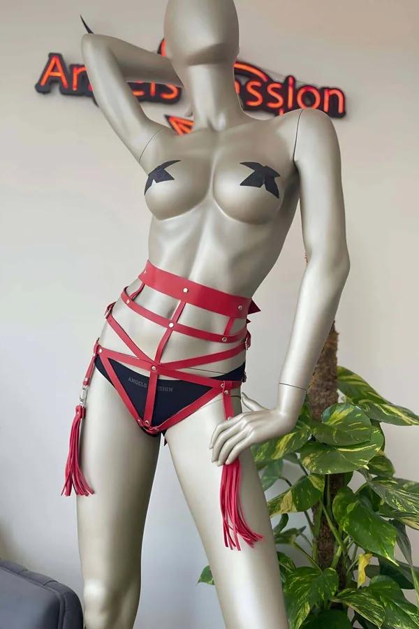 Red faux leather waist harness with crisscross straps silver rivets and tassel garter details on mannequin