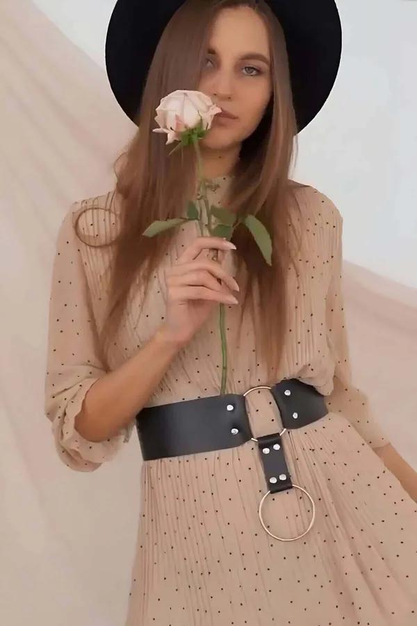 black wide faux leather waist belt with large gold O-ring and silver rivets worn over beige polka-dot dress