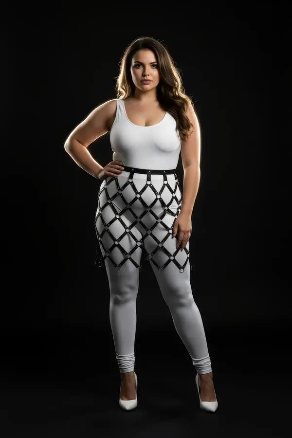 black faux leather diamond lattice skirt overlay harness with silver O-rings worn over white bodysuit and leggings