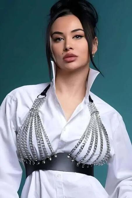 Black faux leather chest harness with cascading silver curb-link chains and stud-trimmed waistband worn over white shirt