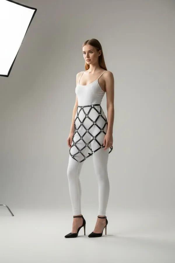 black faux leather diamond grid cage skirt harness with silver O-ring hardware worn over white leggings