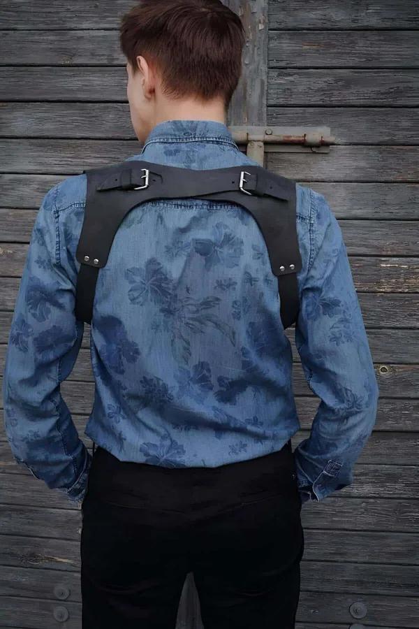 Black faux leather chest harness X-back strap design with silver rectangular buckles worn over denim shirt rear view