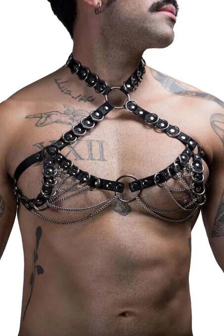 Black faux leather men's chest harness with layered silver chains, dome studs, and dual O-rings on a tattooed male model