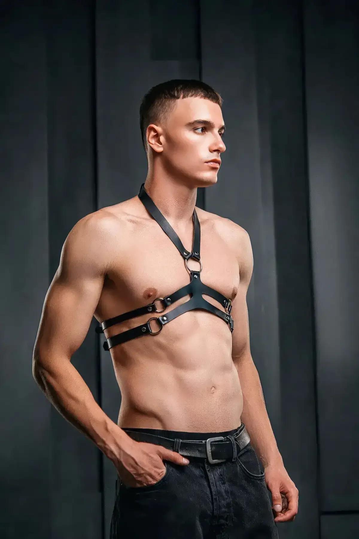 Black faux leather men's chest harness with V-neck strap and triple O-ring hardware across mid-chest bands